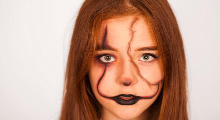 mystical girl with a painted skull on her face in the style of halloween. close up portrait of beautiful girl with fluttering hair. professional halloween makeup